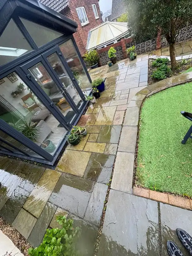 Clean wet sandstone paving wrapping around a corner from a lawn to a set of bifold doors