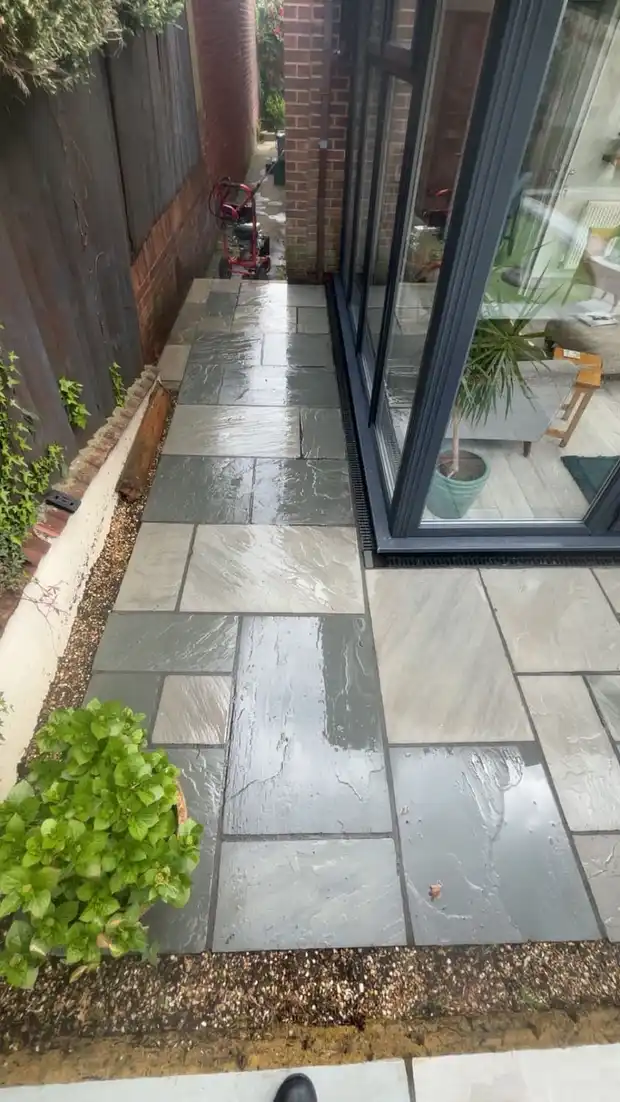Clean grey paving slabs after jet washing, with the pressure washer visible in the background