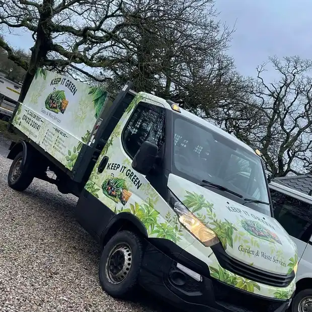 The Keep It Green tipper, wrapped in leaf-green livery, parked under bare oak trees