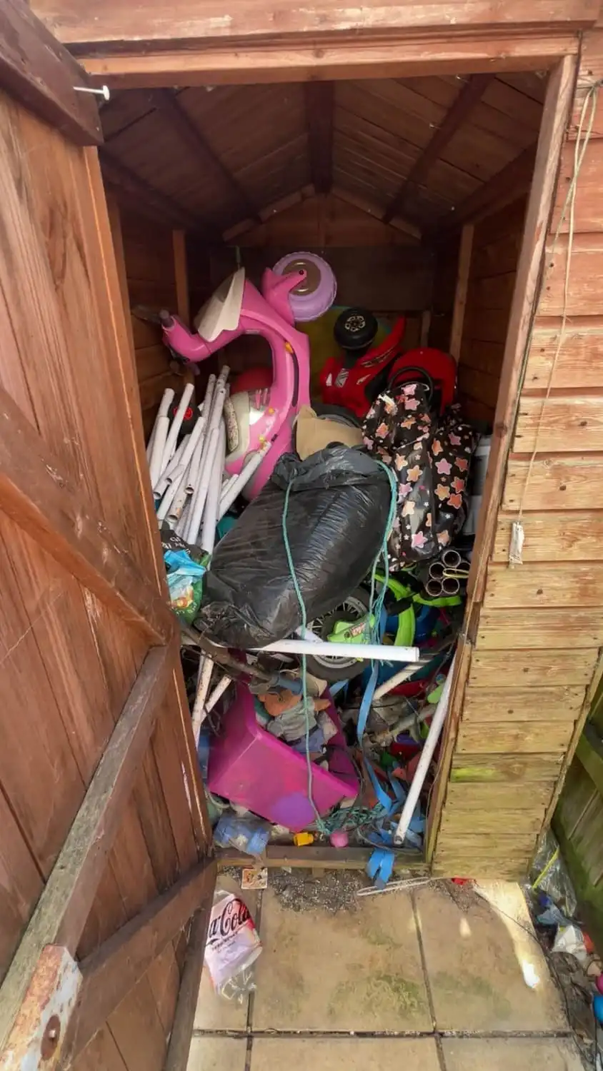 A garden shed packed floor to roof with old toys, bags, pipes and household clutter